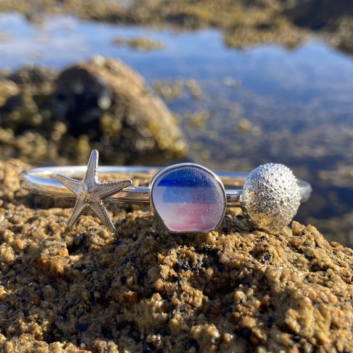 Pink, blue and white English multi colour sea glass solid silver bangle with cast silver sea star and sea urchin by Mornington Sea Glass. Photographed at rock pools on the Mornington  Peninsula, Victoria, Australia.