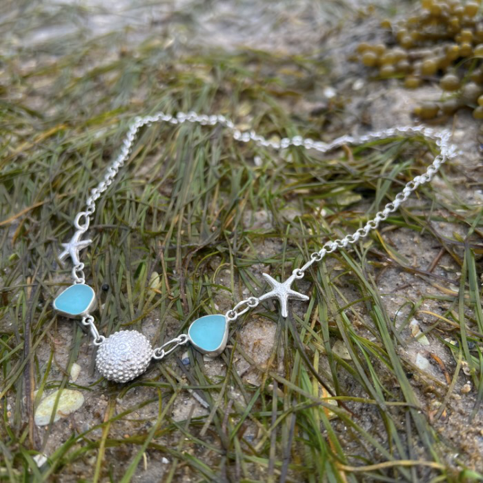 Sterling silver necklace of cast silver sea urchin shells and sea stars and blue sea glass. Hangs on a 42cm sterling silver belcher chain. By Mornington Sea Glass.