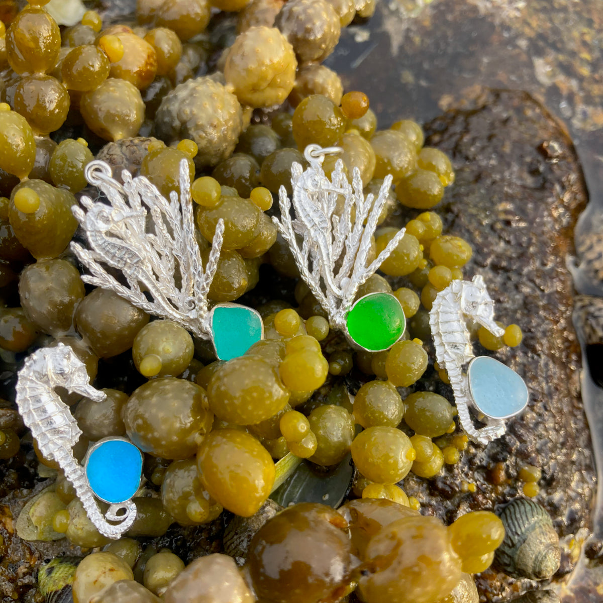 Four sterling silver pendants of seahorses with sea glass in the colours of blue, green and aqua. By Mornington Sea Glass.