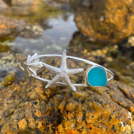 Sterling silver split centre cuff featuring a cast silver limpet shell and sea star as well as ocean teal sea glass gem. 60cm diameter with a 3cm opening.By Mornington Sea Glass.