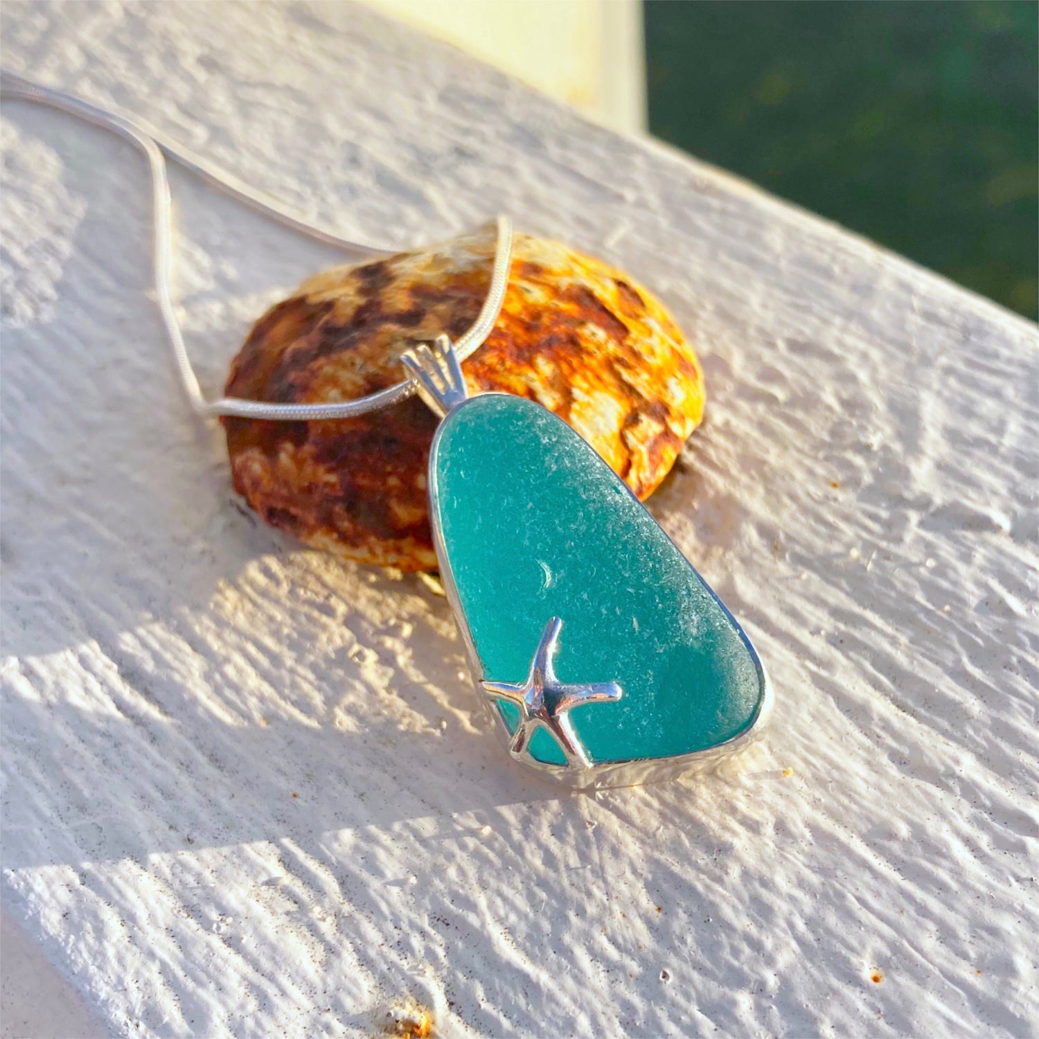 Aqua sea glass pendant with sea star by Mornington Sea Glass. Photographed on a pier on the Mornington Peninsula, Victoria, Australia.