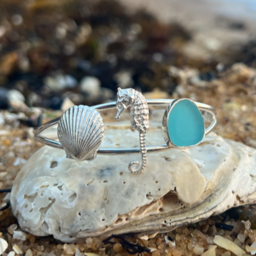 Sterling silver split centre cuff featuring a cast silver scallop shell and seahorse as well a blue sea glass gem. 60cm diameter with a 3cm opening.By Mornington Sea Glass