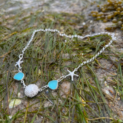 Sterling silver necklace of cast silver sea urchin shells and sea stars and blue sea glass. Hangs on a 42cm sterling silver belcher chain. By Mornington Sea Glass.