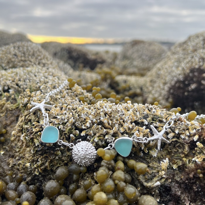 Sterling silver necklace of cast silver sea urchin shells and sea stars and blue sea glass. Hangs on a 42cm sterling silver belcher chain. By Mornington Sea Glass.