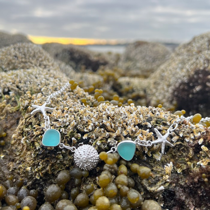 Sterling silver necklace of cast silver sea urchin shells and sea stars and blue sea glass. Hangs on a 42cm sterling silver belcher chain. By Mornington Sea Glass.