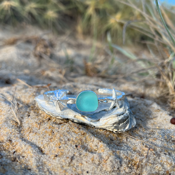 Sterling silver crushed texture cuff featuring a cast silver sea star, shell and an ocean teal sea glass gem. 60cm diameter with a 3cm opening.By Mornington Sea Glass